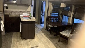 A compact RV kitchen with a microwave, sink, and dining area. - Masood's Lodge (Boulder Creek)