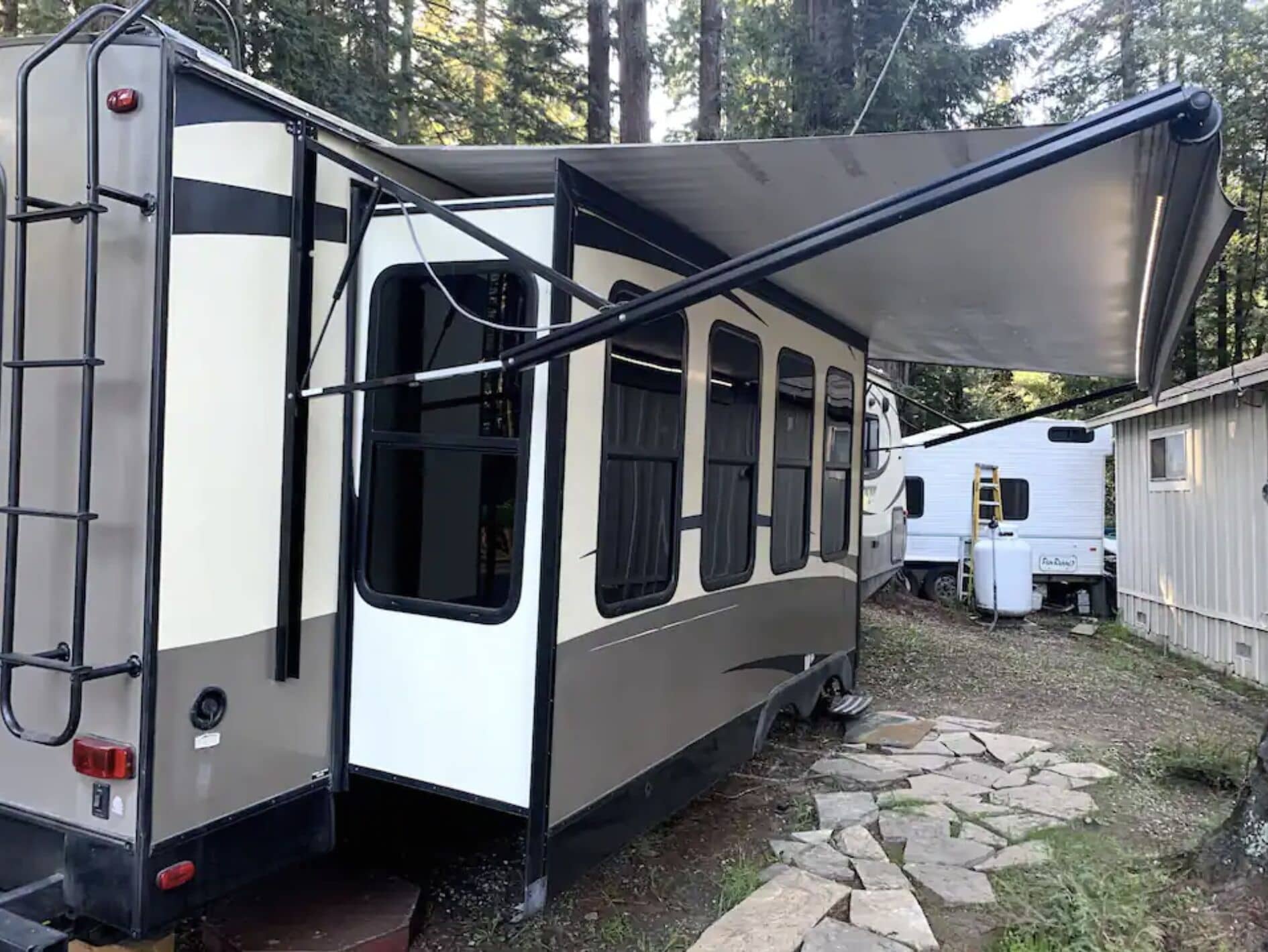 Une maison mobile dotée d’un patio couvert, d’une échelle et d’un réservoir d’eau.