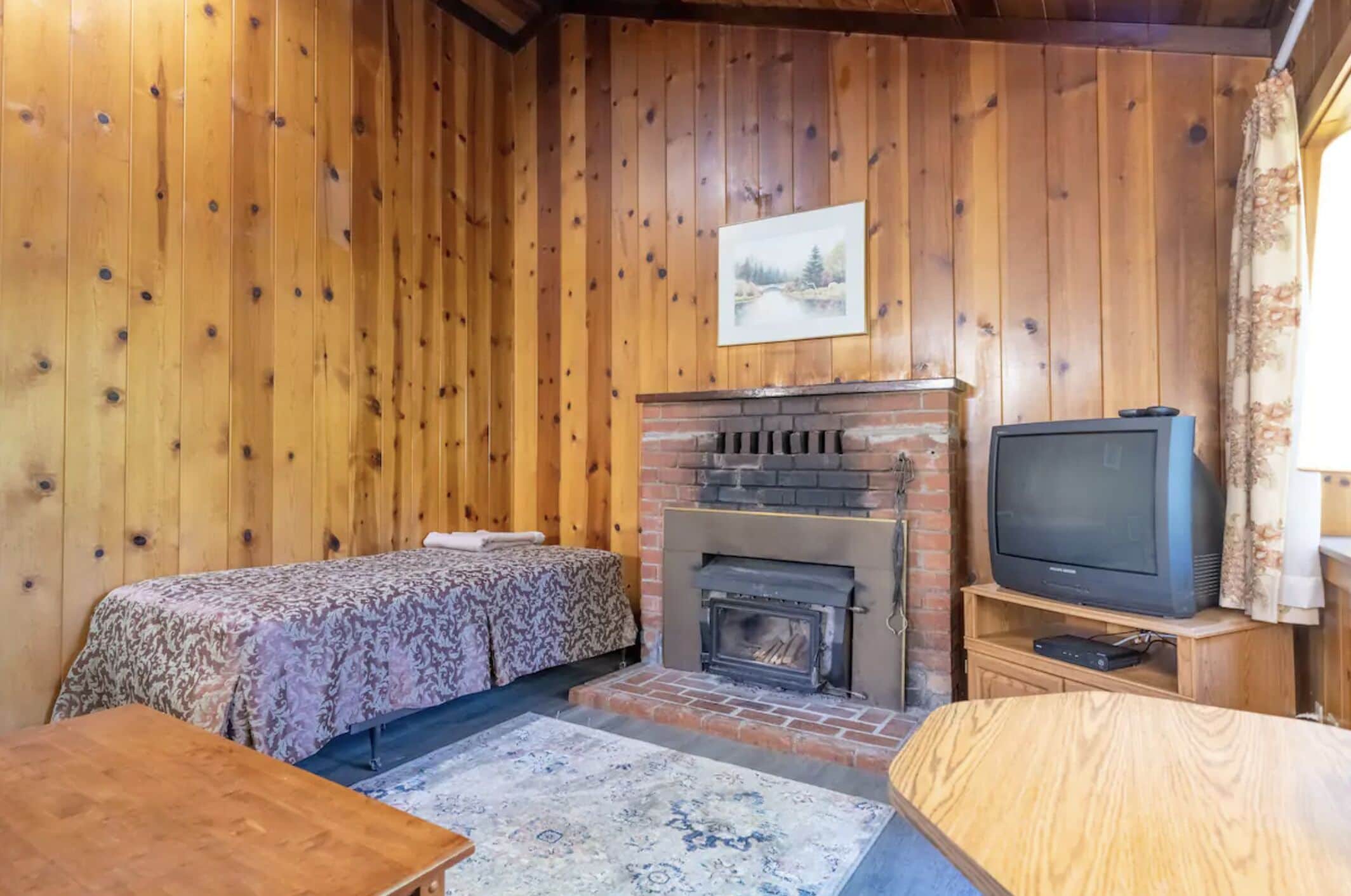 A cozy room with wooden walls, a fireplace, a bed with a patterned bedspread, a television, and a small table.