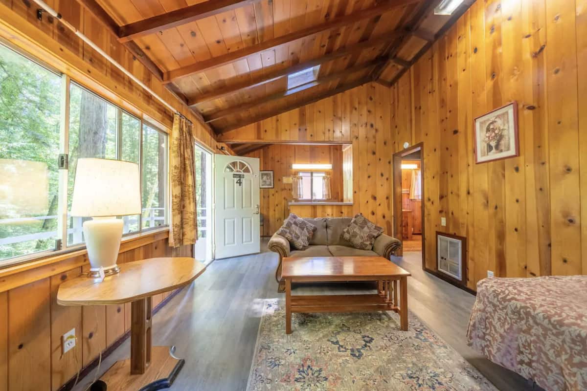 A cozy cabin interior with wooden walls, a sofa, a table, and a bed.