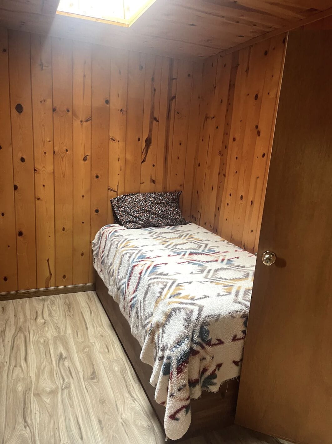 A small, single-bed room with wooden walls and a sloped ceiling.