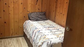 A small, single-bed room with wooden walls and a sloped ceiling.