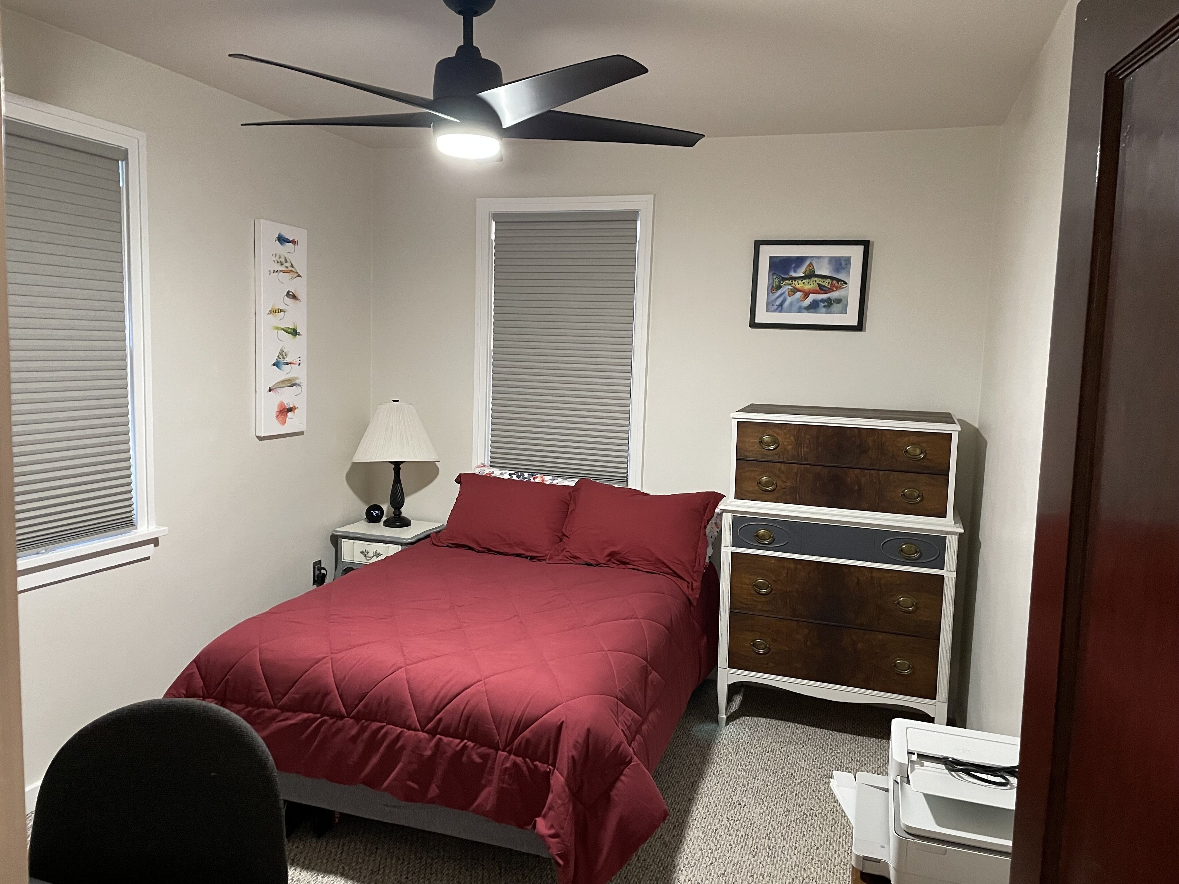 Ein Schlafzimmer mit Bett, Schminktisch, Nachttisch, Lampe und Deckenventilator.