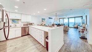 A modern kitchen with white cabinetry, a central island, and a dining area with a view of the ocean. - Luxury Beach Front Condo (Panama City Beach)