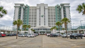 A large hotel with a central entrance, multiple floors, and a parking lot with cars and palm trees. - Luxury Beach Front Condo (Panama City Beach)