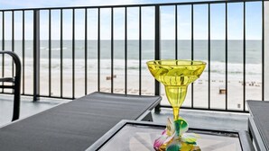A balcony with a glass table and a yellow glass object, overlooking a beach. - Luxury Beach Front Condo (Panama City Beach)