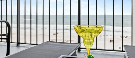 En balkong med ett bord i glas och ett gult glasprydnadsföremål, med utsikt över en strand.