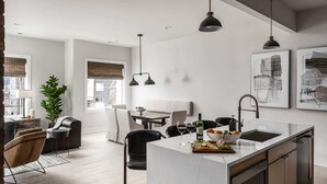 Una cocina moderna con una isla de mármol, iluminación colgante y un comedor con mesa y sillas.