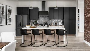 Una cocina moderna con armarios oscuros, salpicadero de mármol y tres taburetes negros.