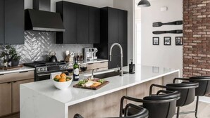 Una cocina moderna con armarios oscuros, una isla de mármol blanco y una pared decorativa de ladrillo.