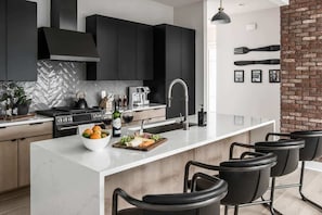 A modern kitchen with dark cabinets, a white marble island, and a brick accent wall.