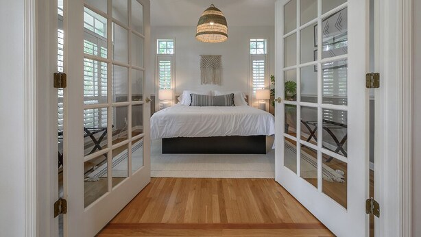 A bedroom with a large bed, white walls, and a wooden floor. - Luxury Harbor Home – Pool, Hot Tub, Basketball Court & Tiki Lounge Near Gulf Beaches (Largo)