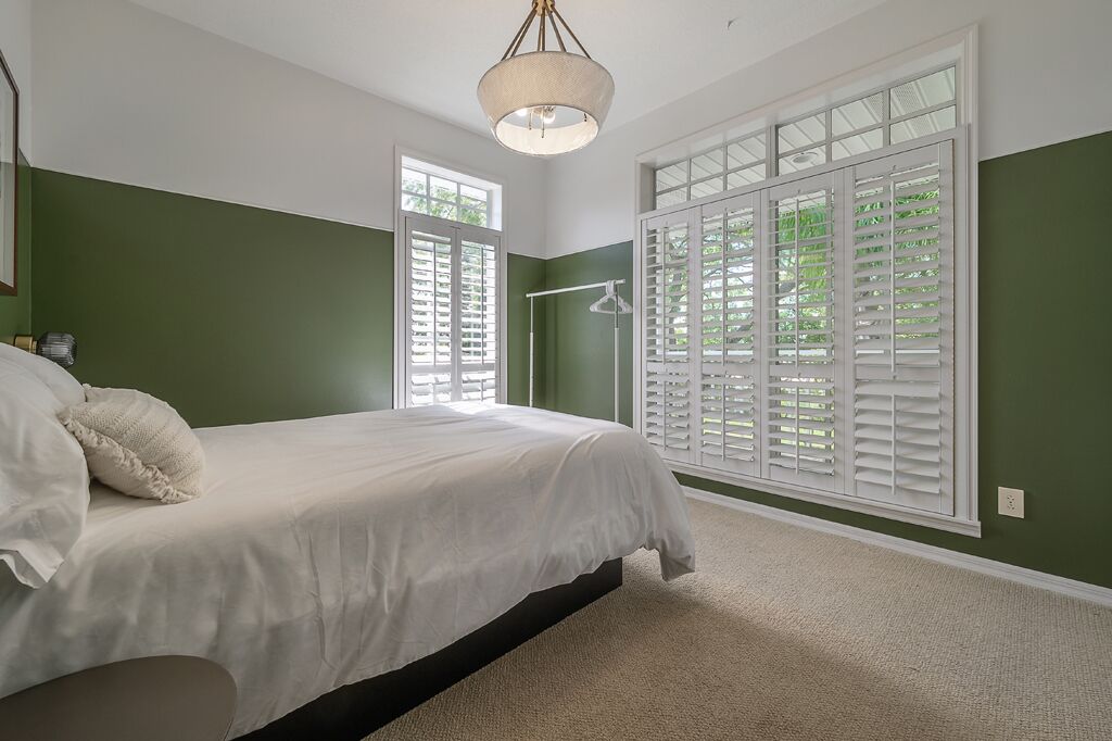 A bedroom with a bed, a hanging light fixture, and large windows with shutters.