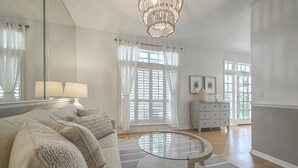 A spacious living room with a round glass coffee table, a beige sofa with throw pillows, a white dresser, and a chandelier. - Luxury Harbor Home – Pool, Hot Tub, Basketball Court & Tiki Lounge Near Gulf Beaches (Largo)