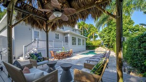 A covered outdoor area with wicker furniture, a pool, and a house in the background. - Luxury Harbor Home – Pool, Hot Tub, Basketball Court & Tiki Lounge Near Gulf Beaches (Largo)