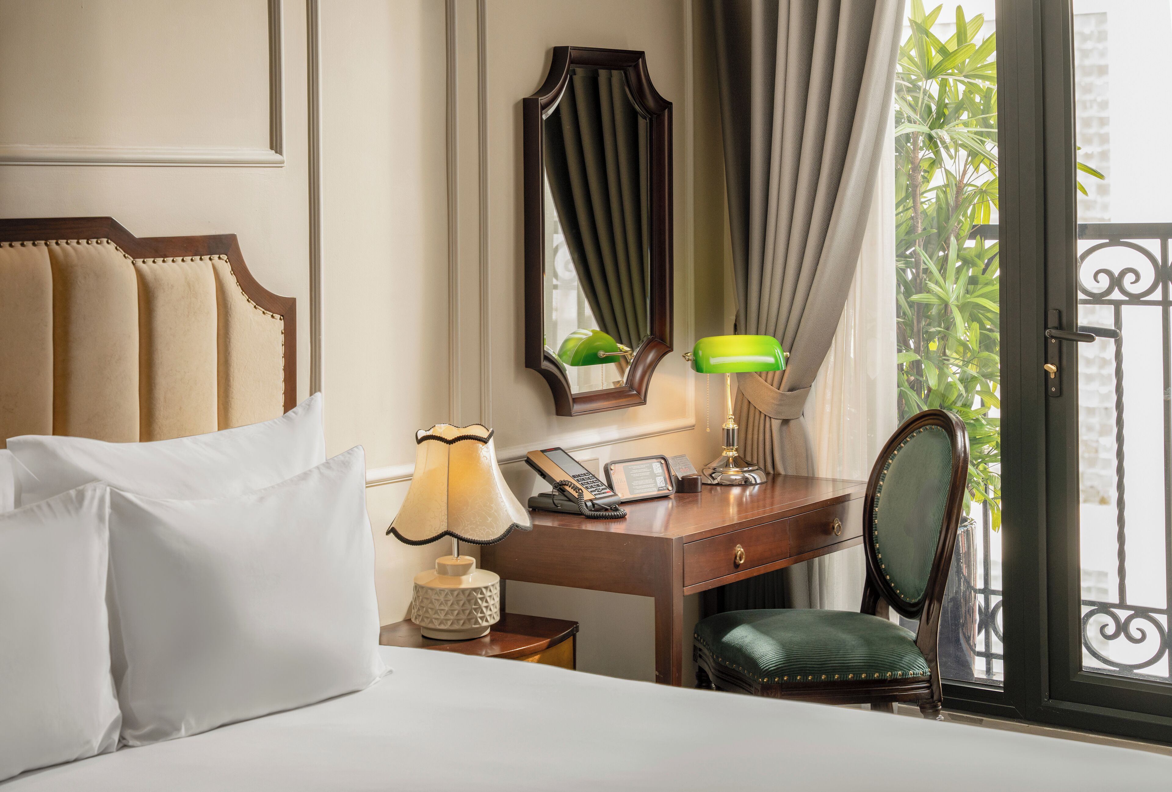 A hotel room with a bed, a desk with a telephone, a lamp, a chair, and a mirror.