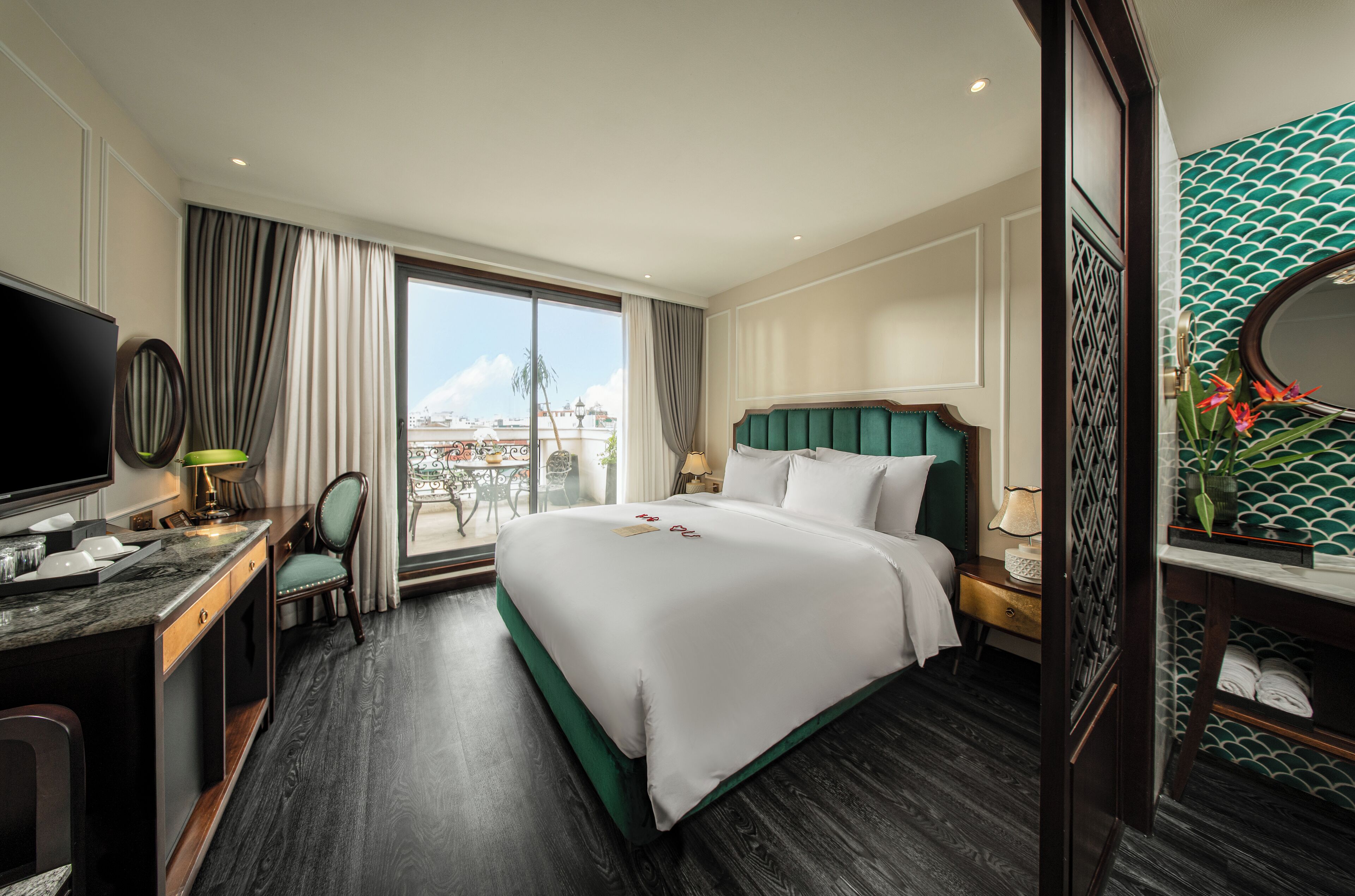 A hotel room with a large bed, a desk with a chair, a television, and a view of the city through the window.
