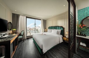 A hotel room with a large bed, a desk with a chair, a television, and a view of the city through the window.