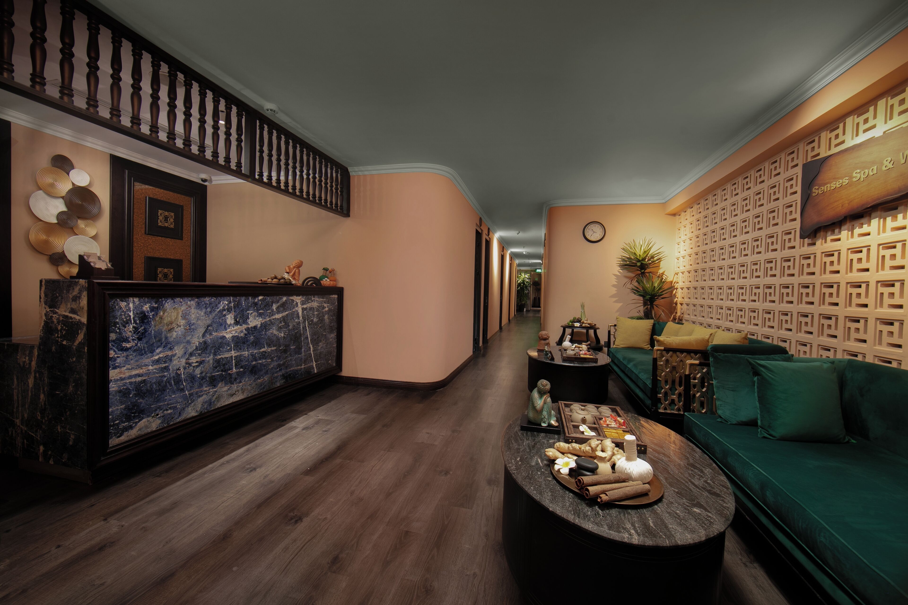 Un hall d’hôtel comprenant un comptoir d’accueil, un canapé vert, une table basse en marbre et un mur orné de motifs.