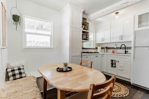 A modern kitchen with white cabinets, a wooden dining table, and a small potted plant.