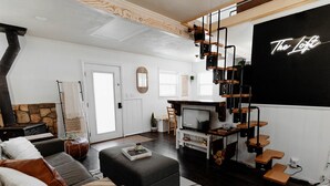 A modern living room with a fireplace, a television, and a loft sign. - Cozy Lakeside Cabin with Hot Tub (Fawnskin)