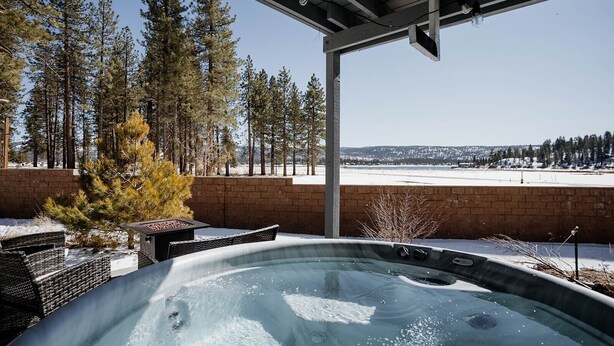 A hot tub in a covered outdoor area with a view of a snowy landscape and tall trees. - Cozy Lakeside Cabin with Hot Tub (Fawnskin)