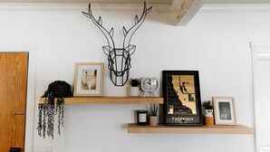 A room with a wooden door, a wall-mounted deer head decoration, a framed picture with text, a clock, and a map of California on a shelf. - Cozy Lakeside Cabin with Hot Tub (Fawnskin)