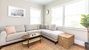 A modern living room with a grey sectional sofa, a wooden coffee table, and a large window with a view of greenery.