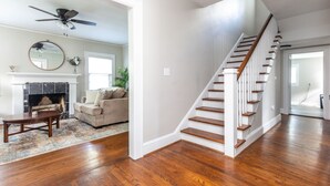 A spacious living room with hardwood flooring, a fireplace, a staircase, and a ceiling fan.