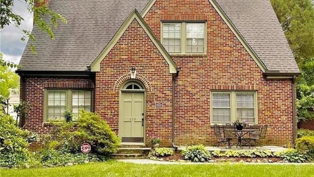 A two-story brick house with a front door, a small porch, and a well-maintained lawn.