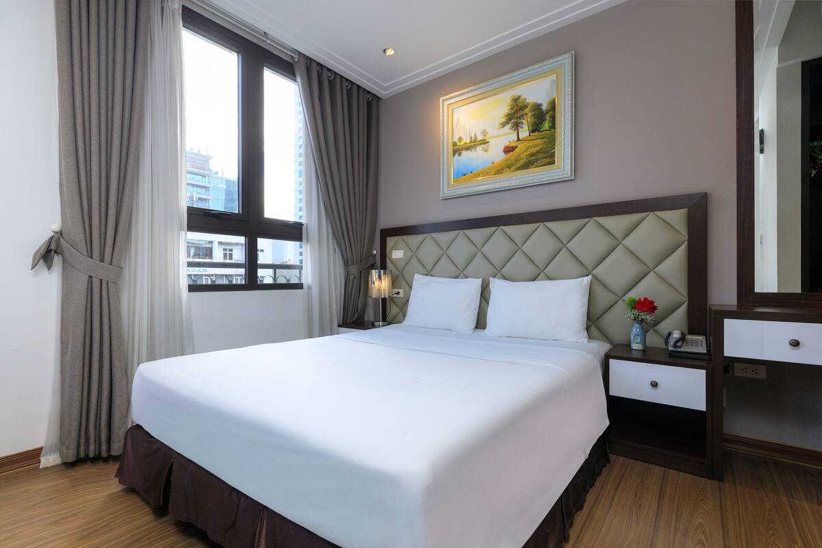 Habitación de hotel con una cama grande, una mesita de noche con lámpara, un aparador y un cuadro en la pared.