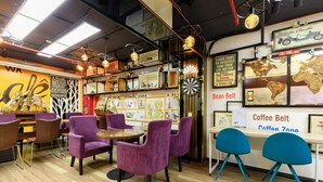 L’intérieur d’un café, avec des chaises violettes et bleues, des tables en bois et diverses décorations, notamment une carte du monde et des tableaux encadrés.