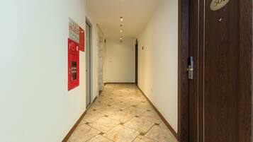 Um corredor com piso ladrilhado, um alarme de incêndio e uma porta com placa de identificação.