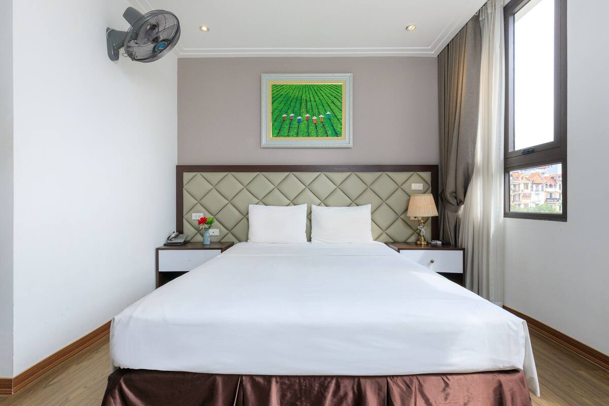 Habitación de hotel con una cama grande, cabecera con diseño de rombos, mesita de noche con lámpara y un cuadro enmarcado en la pared.