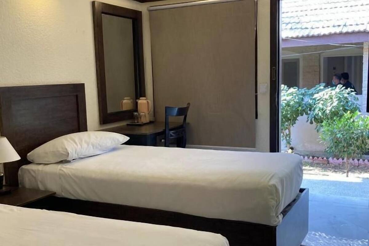 A hotel room with two beds, a large mirror, a chair, and a view of the outside.