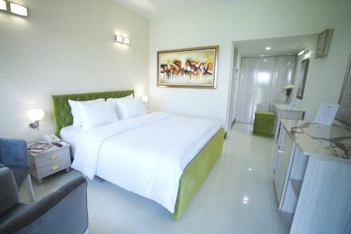 A hotel room with a large bed, a desk, a chair, and a painting on the wall.