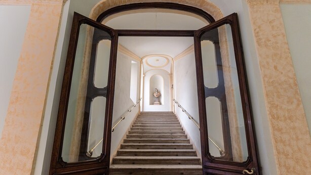 A grand staircase with a handrail, leading to a landing with a statue. - Apartment (Roma)