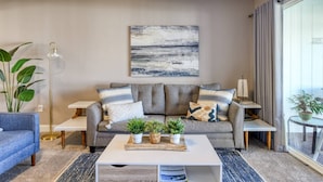 Un salon moderne avec un canapé gris, une table basse blanche et un grand tableau abstrait accroché au mur.