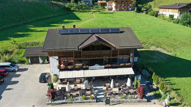 A large building with a sloped roof, outdoor seating area, and a sign reading "FischCafe Bistro Steinberg." - Apartment Steinberg, 2-4 persons, 50 sqm, balcony, TV, 1 bedroom, upper floor (Ramsau bei Berchtesgaden)