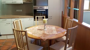 A compact kitchen with white cabinets, a built-in oven, and a dining area with a round table and four chairs. - Apartment Steinberg, 2-4 persons, 50 sqm, balcony, TV, 1 bedroom, upper floor (Ramsau bei Berchtesgaden)
