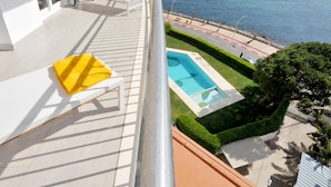 Un balcón con piscina, sillones blancos y vista al mar.