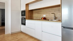 Una cocina moderna con armarios blancos, encimera de madera, electrodomésticos de acero inoxidable y horno empotrado.