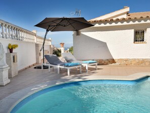 Un espace piscine comprenant deux chaises longues et un parasol, une statue et un mur en pierre.