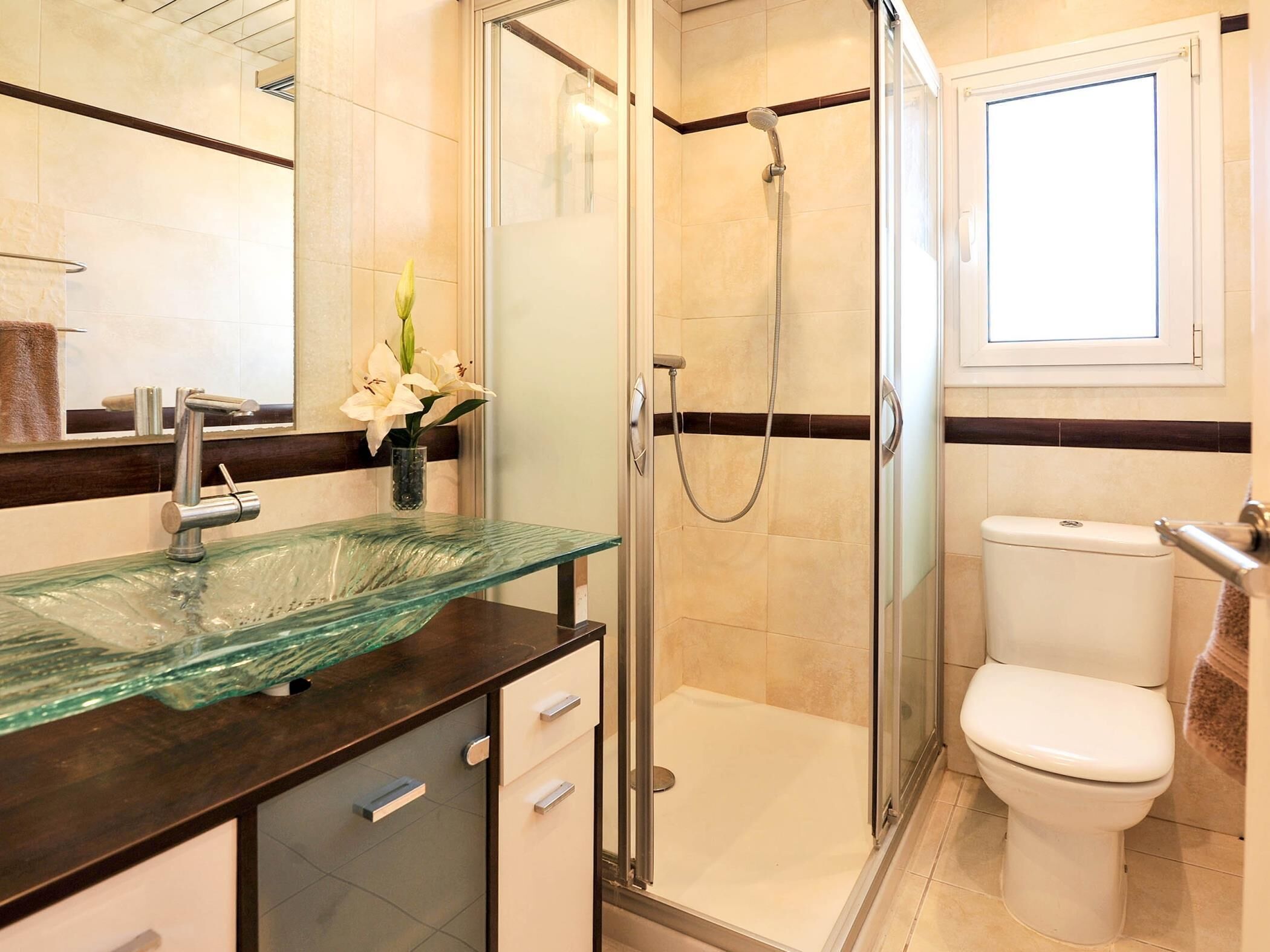 A modern bathroom with a glass sink, a shower, and a toilet.