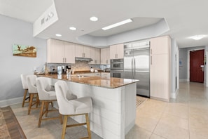 A modern kitchen with a central island, stainless steel appliances, and light-colored cabinetry.