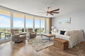 A spacious living room with a view of the ocean, a ceiling fan, and a white sofa.