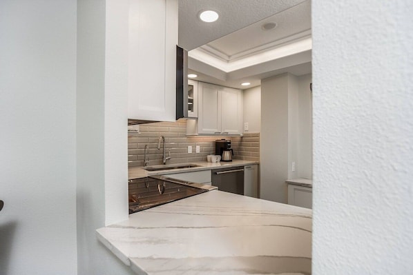 A modern kitchen with white cabinetry, a marble countertop, and a built-in oven.