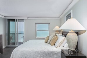 Ein Schlafzimmer mit einem Bett, zwei Nachttischlampen, einem Nachttisch, einem Schminktisch, einem Fenster und einem Balkon mit Blick.