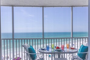 Ein Balkon mit Blick auf den Ozean, ein Tisch mit Tellern und Gläsern sowie zwei Stühle mit Kissen.