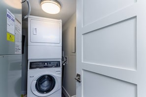 A compact laundry room with a stacked washer and dryer, a door, and a ceiling light fixture.
